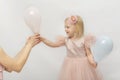 Beautiful girl in lush pink dress smiling takes balloon from hands of woman. Little blonde princess isolated on white background Royalty Free Stock Photo