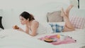 Beautiful girl lying on the bed in morning and chatting, using laptop for that. Young woman eating croissant and typing. Royalty Free Stock Photo