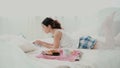 Beautiful girl lying on the bed in morning and chatting, using laptop for that. Young woman eating croissant and typing. Royalty Free Stock Photo