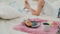 Beautiful girl lying on the bed in morning, using laptop. Young woman eating croissant, typing, browsing the Internet. Royalty Free Stock Photo