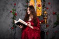 A beautiful girl in a magnificent red dress of the Rococo era stands with a book in her hands against the background of a fireplac Royalty Free Stock Photo