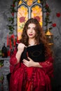 A beautiful girl in a magnificent red dress of the Rococo era stands with a book in her hands against the background of a fireplac Royalty Free Stock Photo