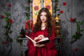 A beautiful girl in a magnificent red dress of the Rococo era stands with a book in her hands against the background of a fireplac Royalty Free Stock Photo