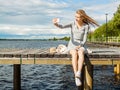 Beautiful girl makes selfie. All alone, she sits on a river pier, the wind spreads blond hair in different directions. Royalty Free Stock Photo