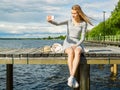 Beautiful girl makes selfie. All alone, she sits on a river pier, the wind spreads blond hair in different directions. Royalty Free Stock Photo