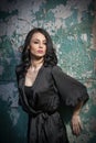 Beautiful girl with makeup posing against old wall with peeling green paint. Pretty brunette in black. Attractive dark hair woman Royalty Free Stock Photo