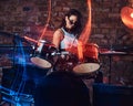 Beautiful girl musician in sunglasses holding the sticks sitting behind the drum set against a brick wall. Royalty Free Stock Photo