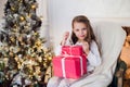 Beautiful girl near Christmas tree unpacking presents sitting on a chair Royalty Free Stock Photo