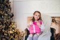 Beautiful girl near Christmas tree unpacking presents sitting on a chair Royalty Free Stock Photo