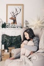 Beautiful girl near fireplace with Christmas tree, candles sits in comfortable armchair. Scandinavian cozy home decor Royalty Free Stock Photo