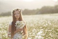 Beautiful woman in a wreath of real flowers, with a bouquet in a field of white daisies Royalty Free Stock Photo