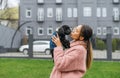 Beautiful girl owner in pink coat holds black curly puppy in her hands and kisses, doggy looks into the camera. Walk with your pet