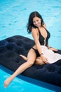 Beautiful girl with perfect figure in a black bikini and hat sitting on a mattress in the swimming pool Royalty Free Stock Photo