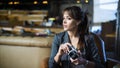 Beautiful girl photographer is holding camera in her hands. Young woman looking at viewfinder and making photo in cafe. Royalty Free Stock Photo