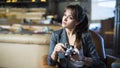 Beautiful girl photographer is holding camera in her hands. Young woman looking at viewfinder and making photo in cafe. Royalty Free Stock Photo