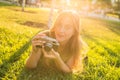 Beautiful girl photographer holds a camera and lying on the grass in the spring outdoors in the park. The concept of Royalty Free Stock Photo