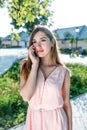 Beautiful girl in pink dress calls on phone, in summer city park, holds smartphone, listens to audio message on Internet Royalty Free Stock Photo