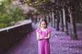 Beautiful girl in pink dress in cherry blossom park on a spring day, flower petals falling from the tree