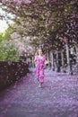 Beautiful girl in pink dress in cherry blossom park on a spring day, flower petals falling from the tree