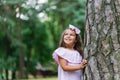 A beautiful girl in a pink dress stands near a tree in the forest in summer, smiling and dreaming Royalty Free Stock Photo