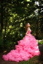 Beautiful girl in pink evening dress with fluffy skirt is posing in botanical garden on the grass surrounded by the woods Royalty Free Stock Photo