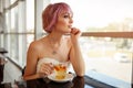 A beautiful girl with pink painted hair sits in a restaurant near the window drinking fruit tea and looking dreamily forward. Royalty Free Stock Photo