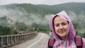 Beautiful girl with a pink sports jacket, backpack, transparent raincoat, with drops on a bridge in Montenegro