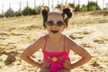 A beautiful girl in a pink swimsuit and glasses is sitting on a sandy beach and laughing Royalty Free Stock Photo