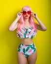Beautiful girl in a pink wig and colored bikini posing on a yellow background. Woman with artificial long hair and pink Royalty Free Stock Photo