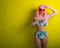 Beautiful girl in a pink wig and colored bikini posing on a yellow background. Woman with artificial long hair and pink Royalty Free Stock Photo