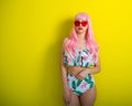 Beautiful girl in a pink wig and colored bikini posing on a yellow background. Woman with artificial long hair and pink Royalty Free Stock Photo