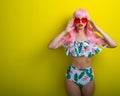 Beautiful girl in a pink wig and colored bikini posing on a yellow background. Woman with artificial long hair and pink Royalty Free Stock Photo