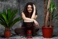 Beautiful girl playing drum in tropical plants over grey background. Royalty Free Stock Photo