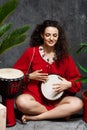 Beautiful girl playing drum in tropical plants over grey background. Royalty Free Stock Photo