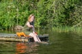 Beautiful girl plays with water sitting on a wooden jetty at a l Royalty Free Stock Photo