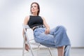 Beautiful girl posing on a white background sitting on a chair in a black bodysuit and jeans. Underwear advertising concept Royalty Free Stock Photo
