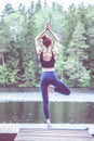 Beautiful girl practicing yoga Tree pose, Vrikshasana on the lake. The concept of appeasement, healthy lifestyle