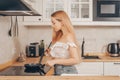 Beautiful girl prepares food on an induction stove. A woman prepares breakfast in a frying pan. The blonde in the bright kitchen