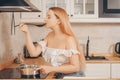 Beautiful girl prepares food on an induction stove. A woman cooks soup or sauce in a saucepan. The blonde in the bright kitchen