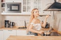 Beautiful girl prepares food on an induction stove. A woman cooks soup or sauce in a saucepan. The blonde in the bright kitchen