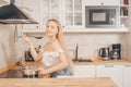 Beautiful girl prepares food on an induction stove. A woman cooks soup or sauce in a saucepan. The blonde in the bright kitchen