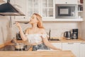 Beautiful girl prepares food on an induction stove. A woman cooks soup or sauce in a saucepan. The blonde in the bright kitchen