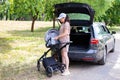 A beautiful girl puts a baby stroller into the open trunk of a car. Family car concept. Sunny weather in summer.