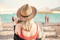 Beautiful girl in a red bikini and straw hat on the beach. Back view. White sand, blue water and beach umbrellas on the Royalty Free Stock Photo