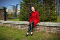 Beautiful girl in a red coat sitting on a brick parapet