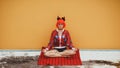 Beautiful girl in red devil costume sitting in yoga pose in anticipation of Halloween. Wears a red wig and horns. The