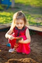 Beautiful girl red dress plays in sandbox. child safety on the playground. Royalty Free Stock Photo