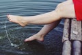 Beautiful girl in red dress is sitting on the wooden pier. Woman is dangling her feet into the lake. Rustic and natural photo