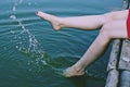 Beautiful girl in red dress is sitting on the wooden pier. Woman is dangling her feet into the lake. Rustic and natural photo