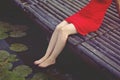 Beautiful girl in red dress is sitting on the wooden pier. Woman is dangling her feet into the lake. Rustic and natural photo Royalty Free Stock Photo